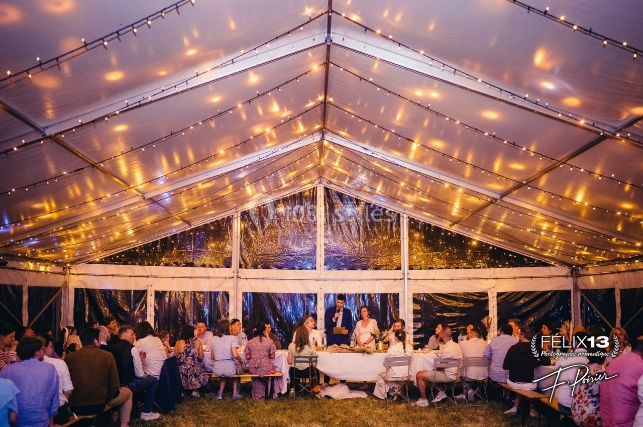 Dîner festif sous une tente éclairée de guirlandes lumineuses, avec des invités assis autour de tables.