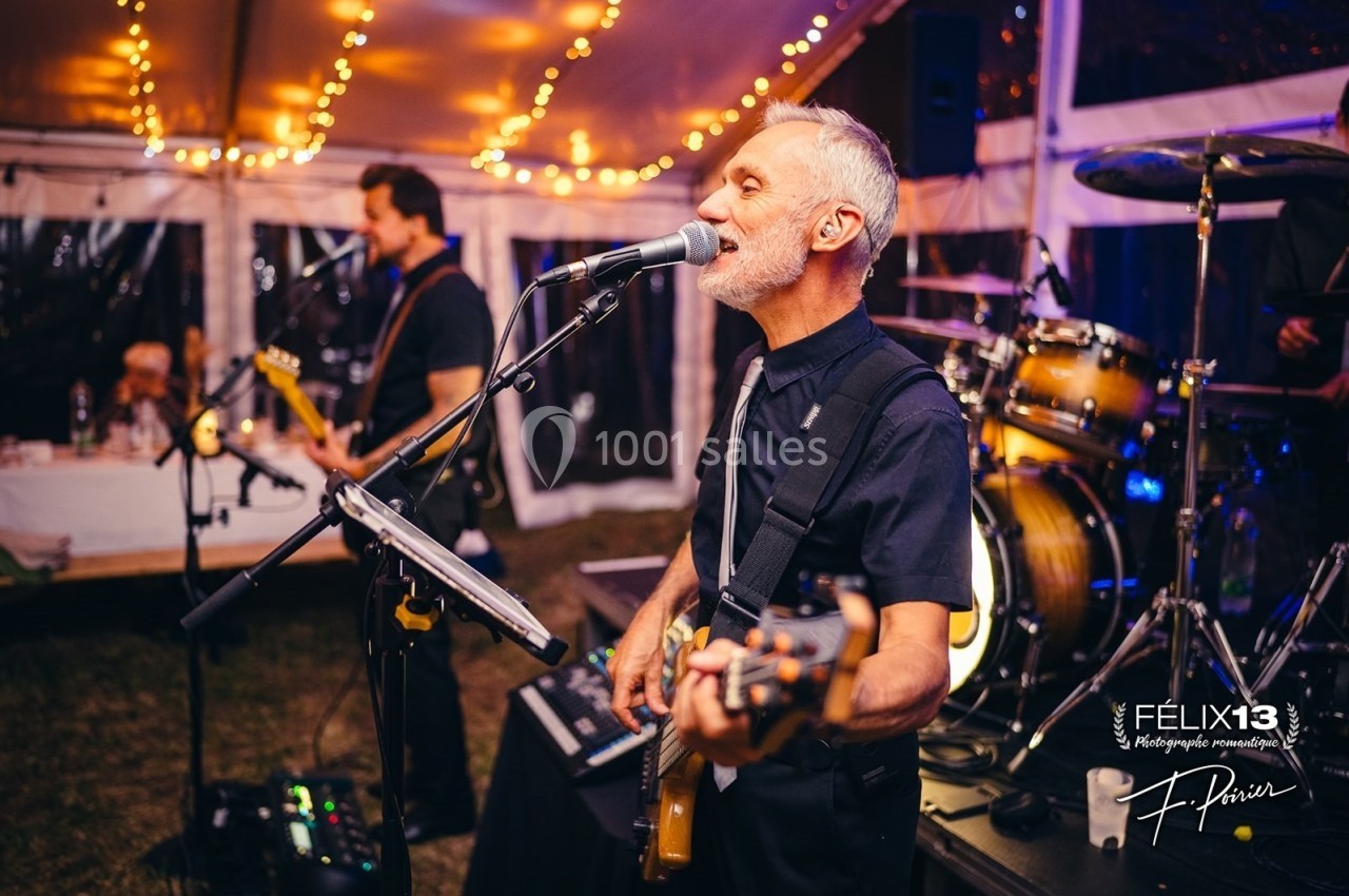 Un groupe de musiciens joue en live sous une tente éclairée par des guirlandes lumineuses.
