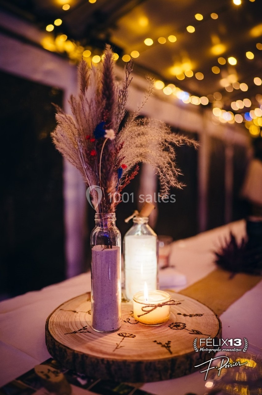 Bouquet de fleurs séchées dans un vase en verre, bougie allumée et décor rustique sur une table éclairée.