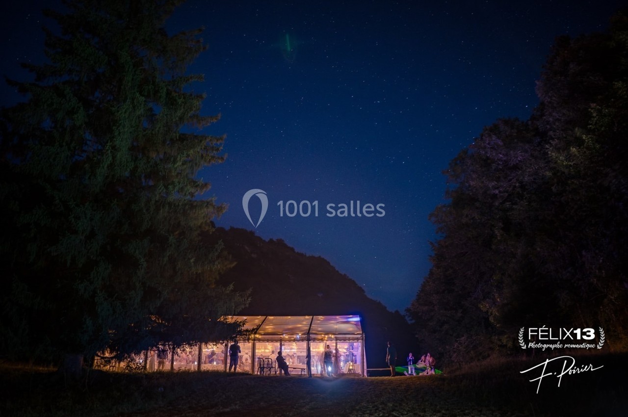 Vue nocturne d'une tente éclairée au milieu d'un paysage boisé sous un ciel étoilé.