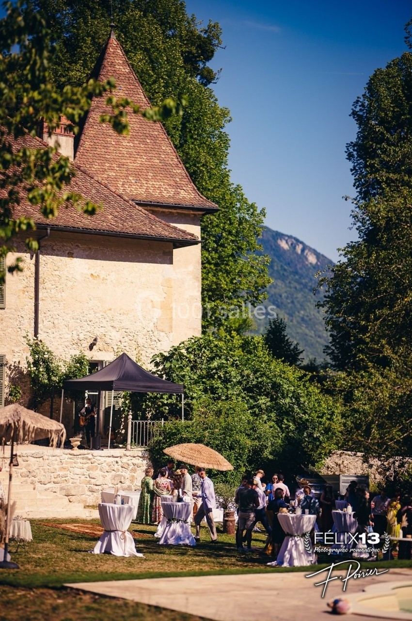 Groupe de personnes rassemblées dans un jardin près d'un bâtiment ancien avec des arbres et des montagnes en arrière-plan.