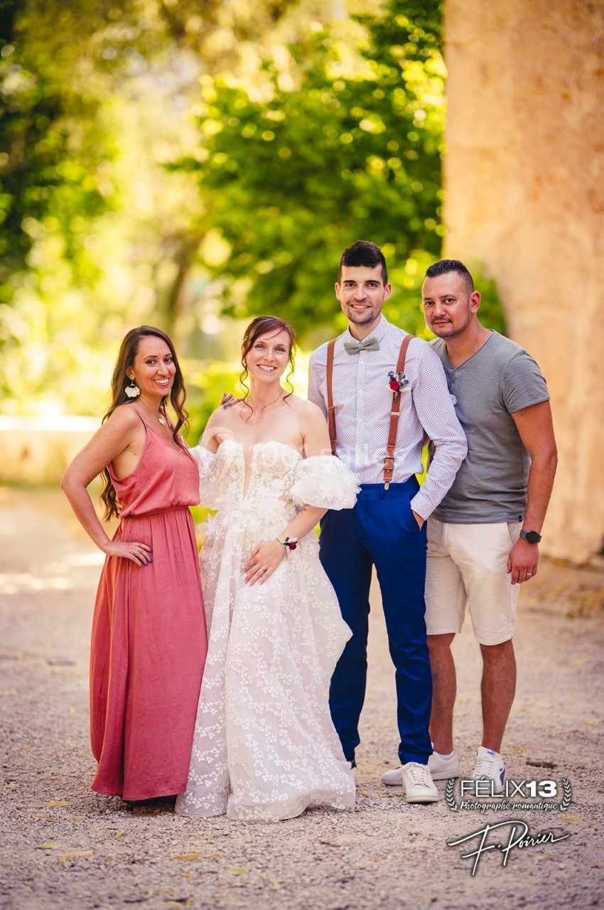 Quatre personnes posent ensemble en extérieur, dont une mariée en robe blanche et un homme en tenue élégante.