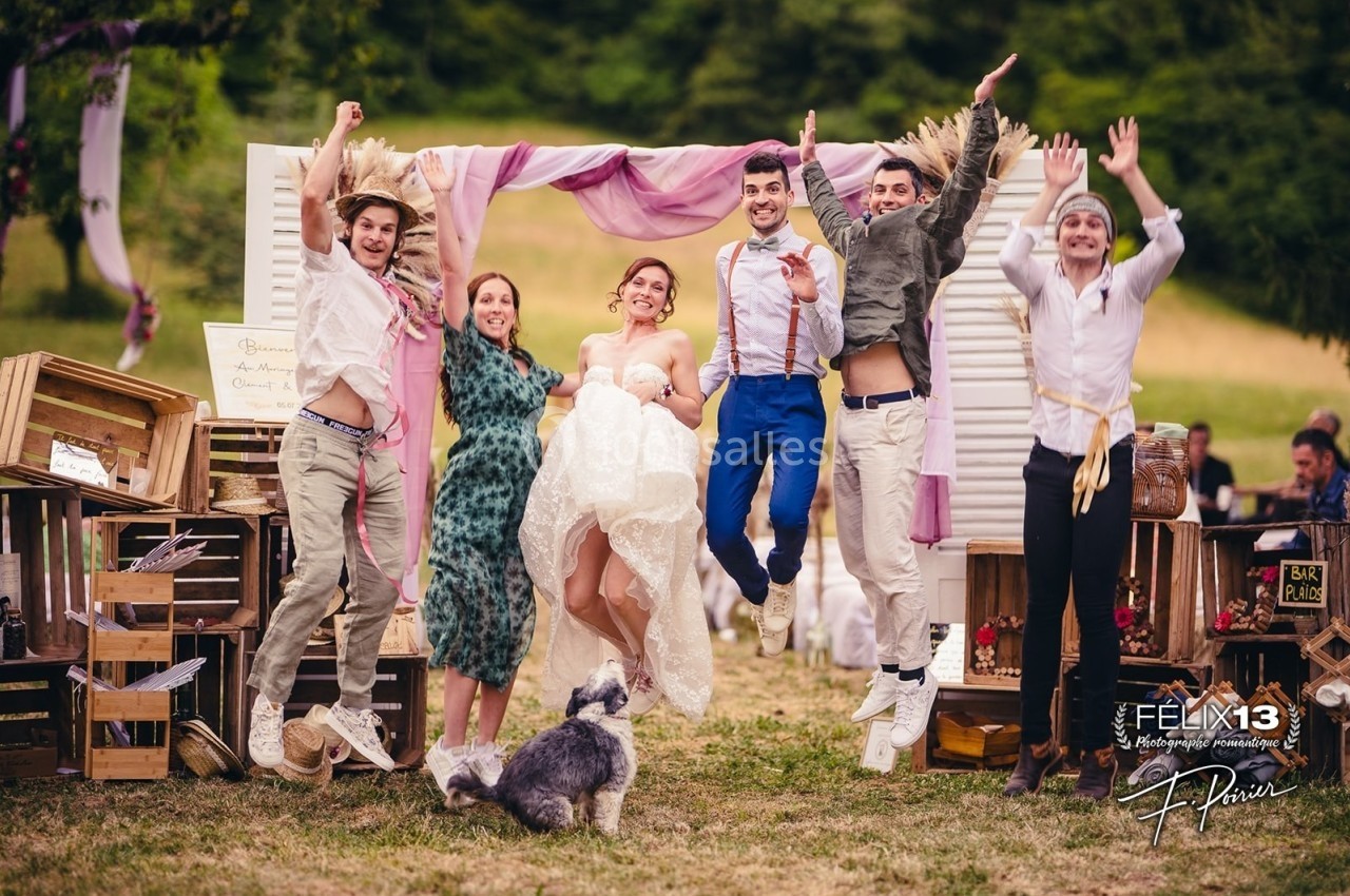 Un groupe de personnes souriantes saute joyeusement devant une arche décorée lors d'un événement en plein air.