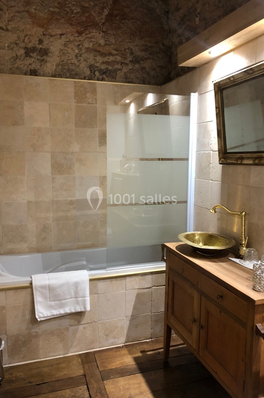 Salle de bain avec baignoire, paroi vitrée, vasque dorée sur meuble en bois et miroir encadré.