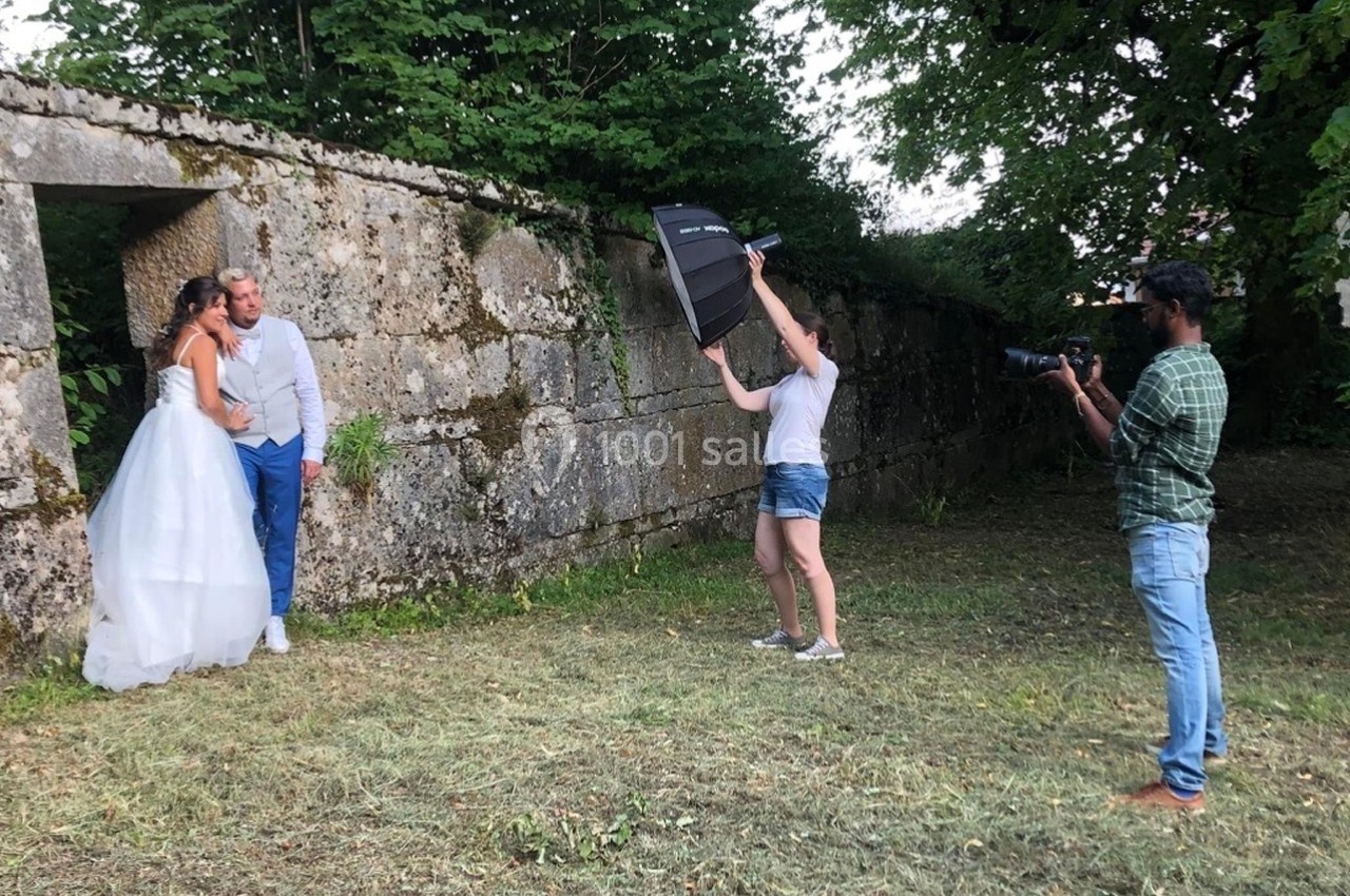 Un couple pose pour une séance photo de mariage en extérieur, avec un photographe et un assistant tenant un réflecteur.