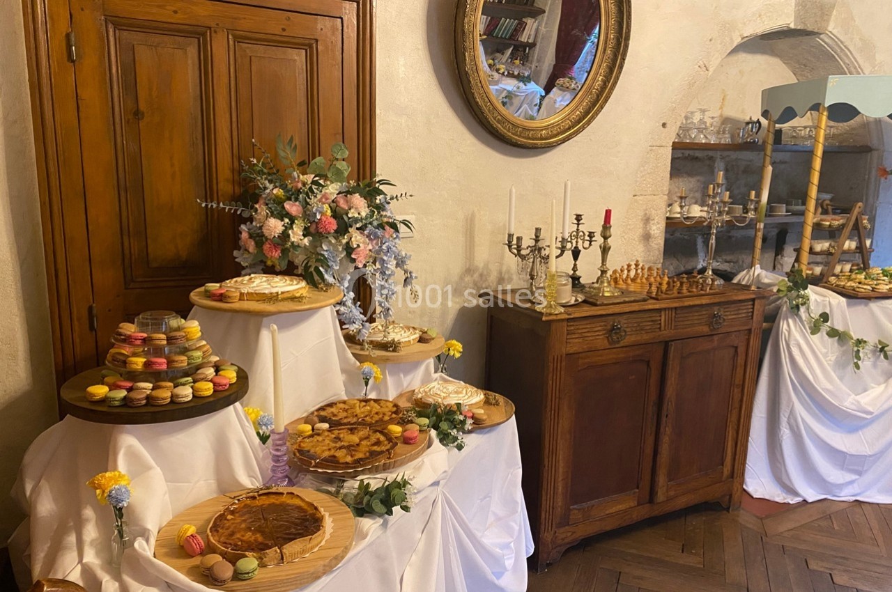 Buffet de desserts avec tartes, macarons et décor floral dans une pièce au style rustique avec meubles anciens.