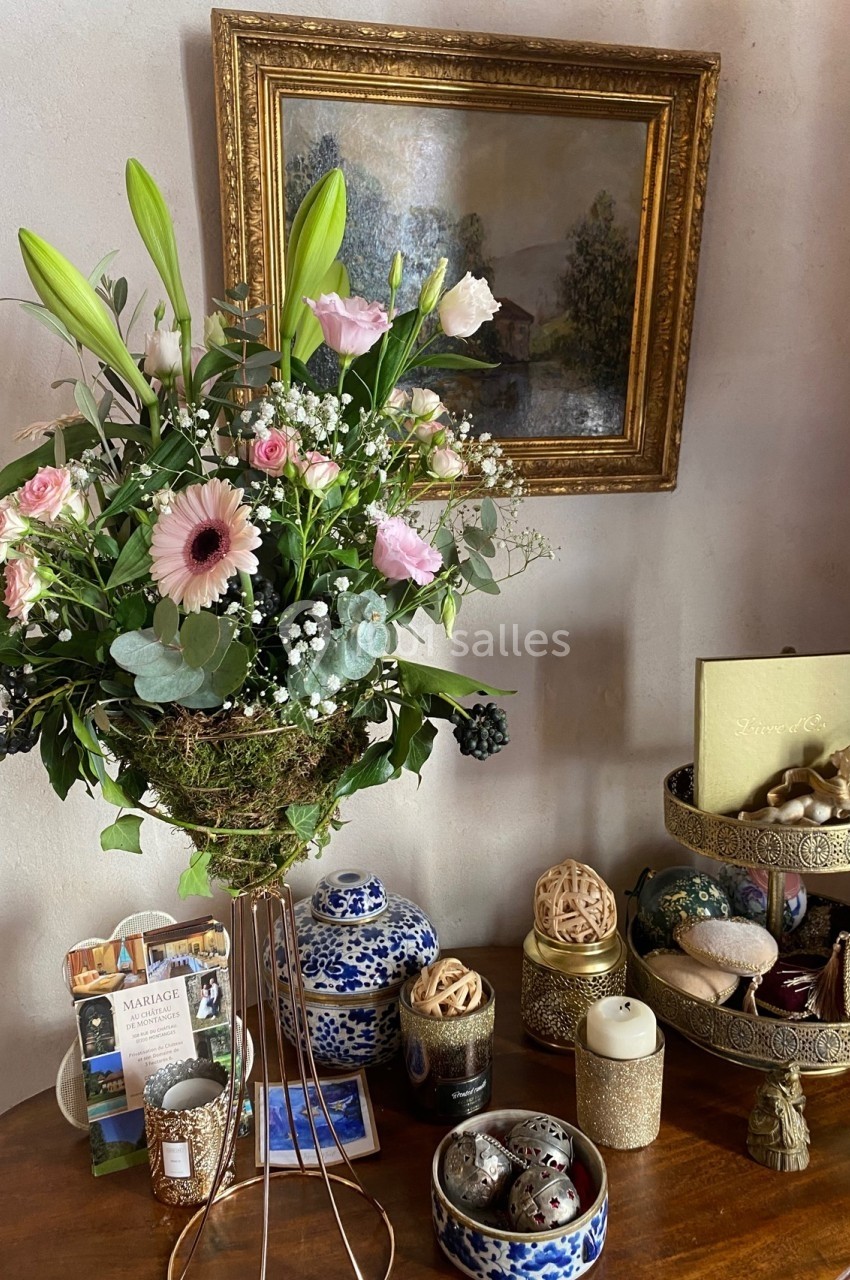 Bouquet de fleurs roses et blanches sur pied en métal, posé sur une table avec objets décoratifs et tableau en arrière-plan.