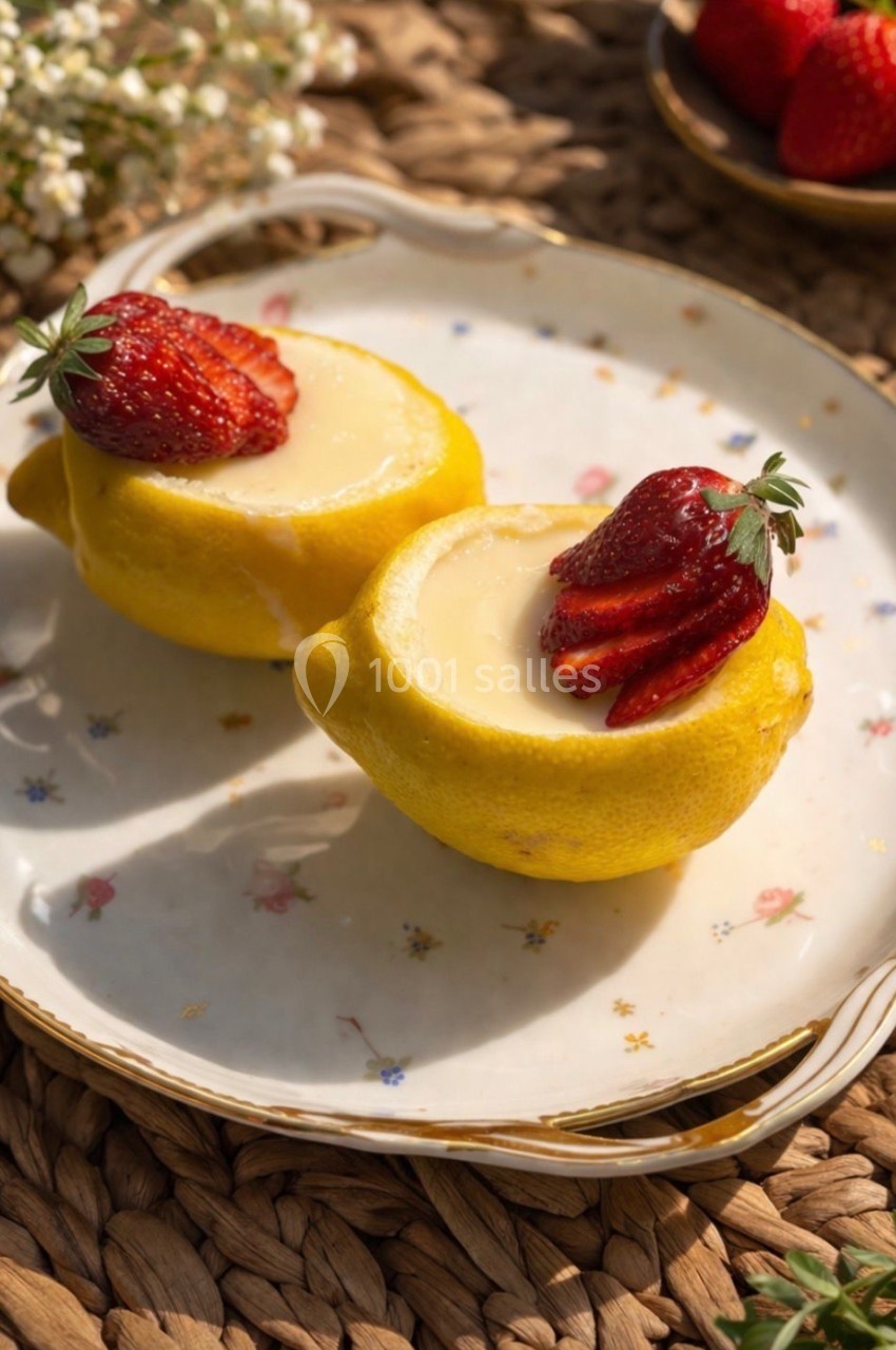 Deux citrons évidés remplis de crème, garnis de fraises, présentés sur une assiette décorative.