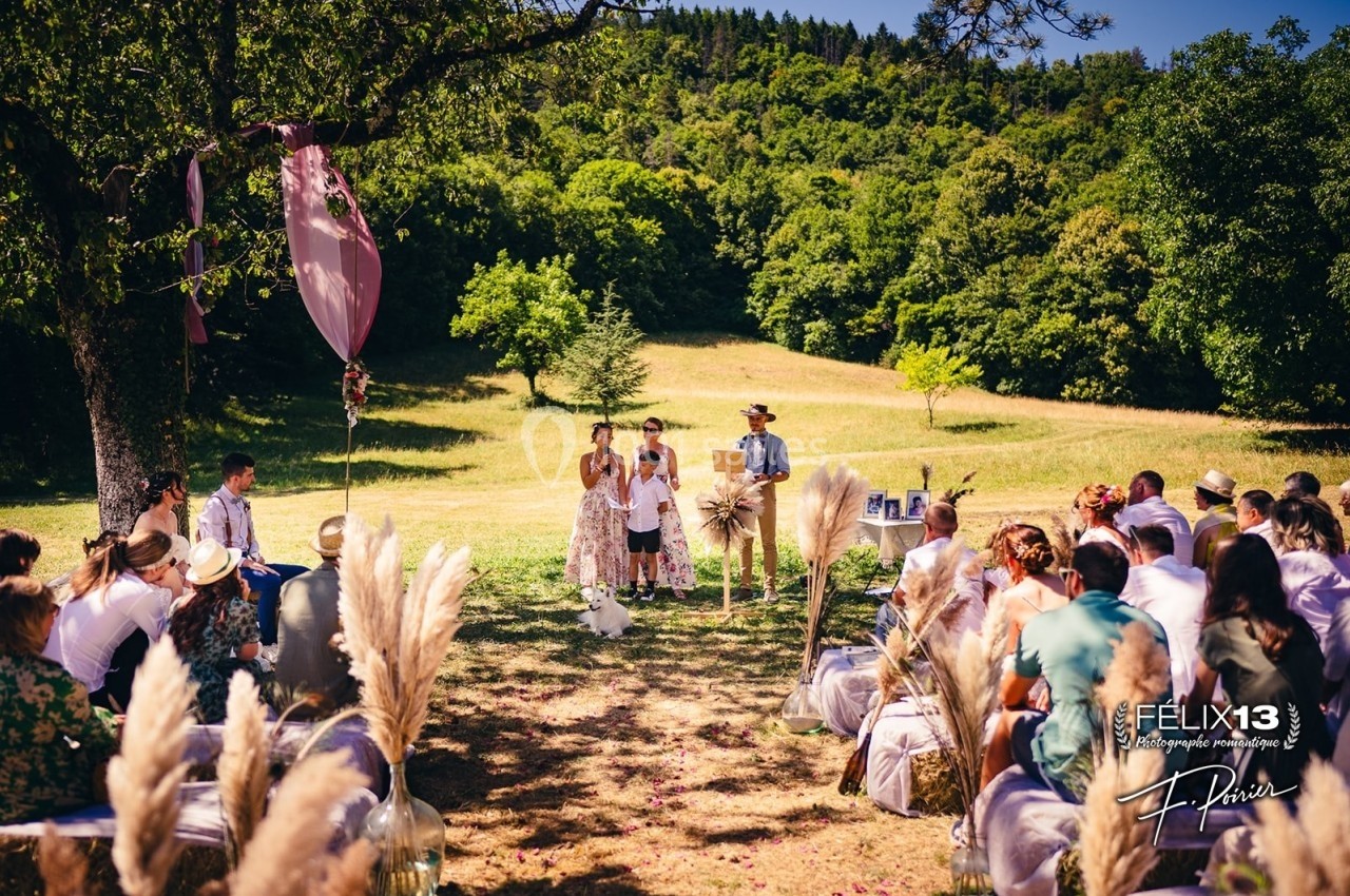 Cérémonie en plein air avec des invités assis, un couple et un enfant au centre, entourés de décorations naturelles.