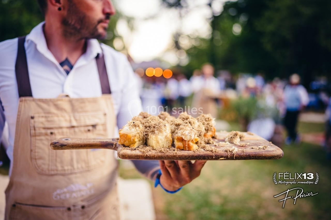 Un homme en tablier présente un plateau de toasts garnis, en extérieur lors d'un événement.