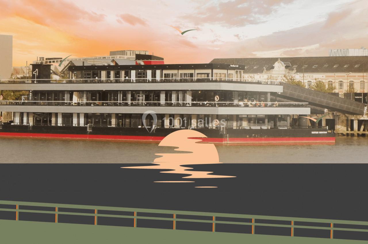 Bateau moderne amarré sur un fleuve au coucher du soleil, avec des bâtiments en arrière-plan.