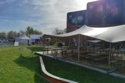 Salle lumineuse avec de grandes baies vitrées, tables dressées avec nappes grises, vaisselle et décoration florale.