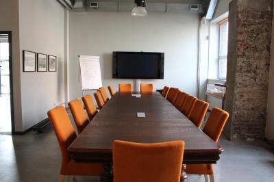 Salle lumineuse avec de grandes baies vitrées, tables dressées avec nappes grises, vaisselle et décoration florale.