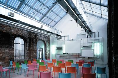 Salle lumineuse avec de grandes baies vitrées, tables dressées avec nappes grises, vaisselle et décoration florale.