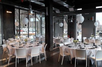 Salle lumineuse avec de grandes baies vitrées, tables dressées avec nappes grises, vaisselle et décoration florale.