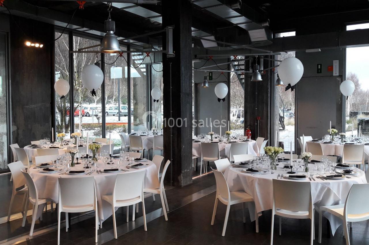 Salle de réception moderne avec tables rondes dressées, nappes blanches et décorations de ballons.