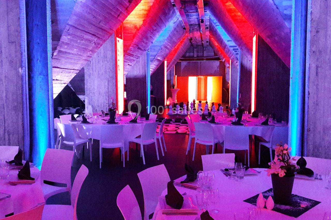 Salle de réception avec tables dressées, éclairage coloré rouge et bleu, et ambiance moderne.