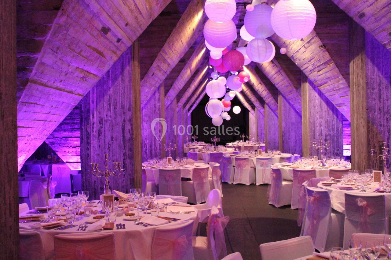 Salle de réception décorée avec des tables dressées et des lanternes suspendues sous une charpente en bois éclairée en…