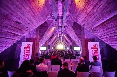 Salle lumineuse avec de grandes baies vitrées, tables dressées avec nappes grises, vaisselle et décoration florale.