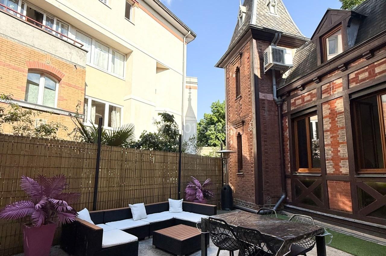 Cour extérieure avec salon de jardin, table et chaises, entourée de bâtiments en briques et d'une clôture en bambou.