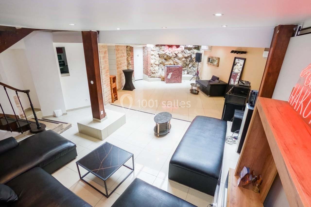 Salon spacieux avec canapés en cuir noir, table basse, murs en pierre et espace ouvert lumineux.