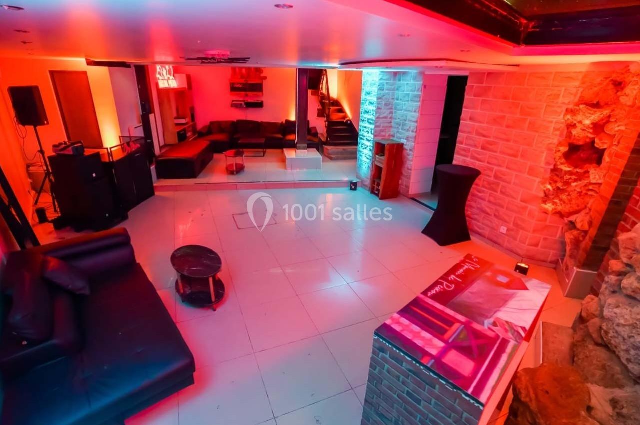 Salle moderne avec éclairage coloré, murs en pierre, canapés noirs, miroirs et comptoir en briques.