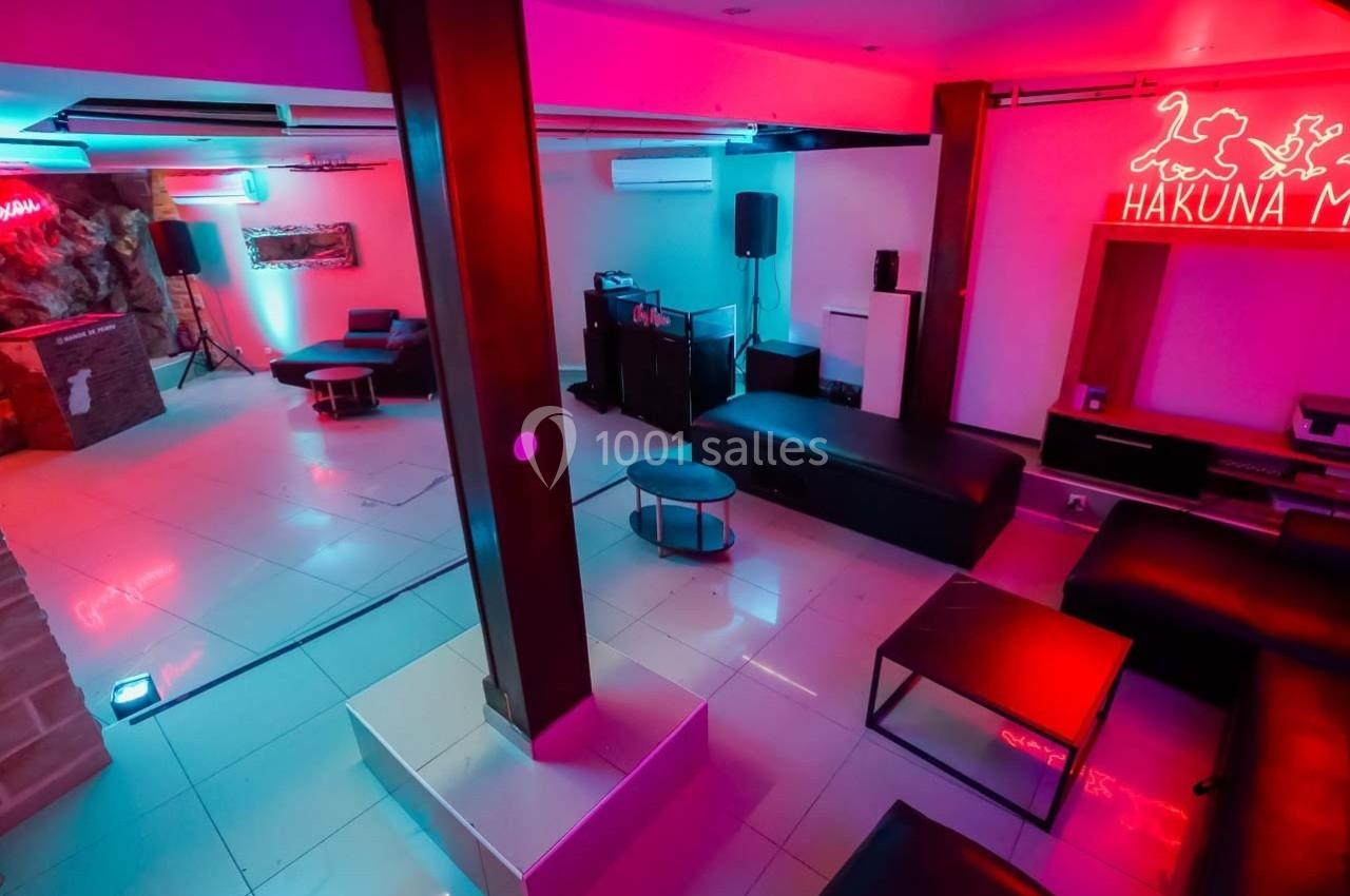 Salle moderne avec éclairage néon coloré, mobilier minimaliste et espace ouvert comprenant des sièges et une petite scène.