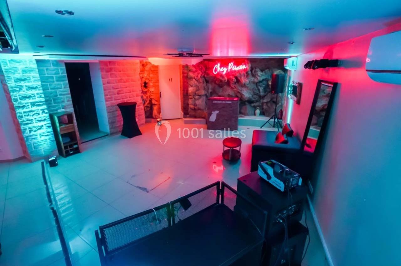 Salle moderne éclairée par des lumières rouges et bleues, avec un comptoir, des fauteuils et un décor en pierre.