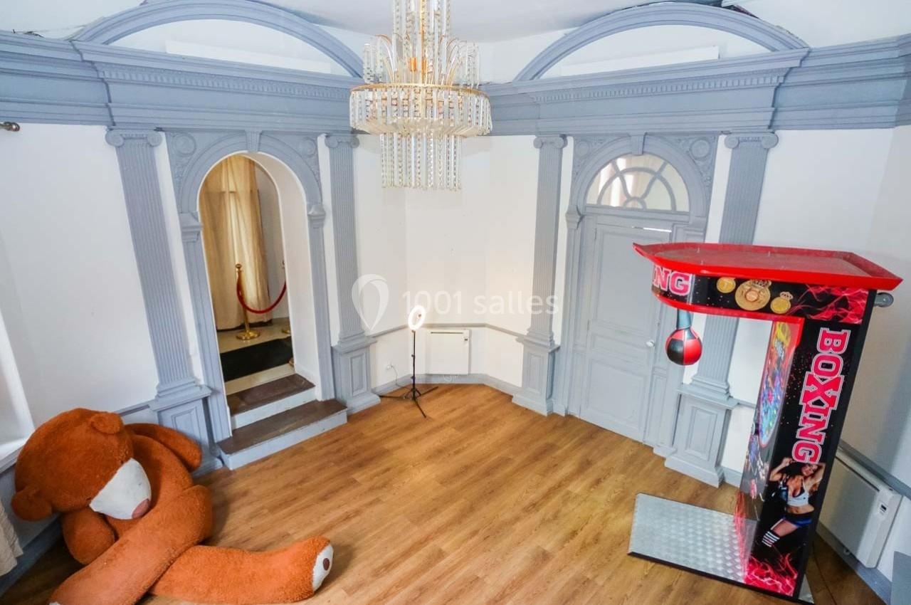 Salle avec un grand ours en peluche, un sac de boxe suspendu et un décor intérieur classique avec moulures grises.