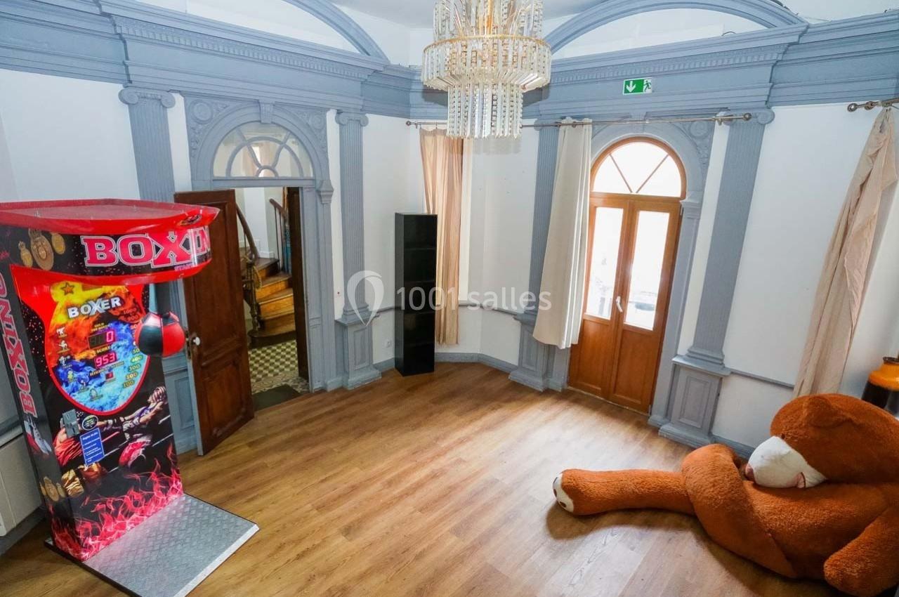 Salle avec un sol en bois, un jeu de boxe coloré, un grand ours en peluche et des fenêtres à arcs.