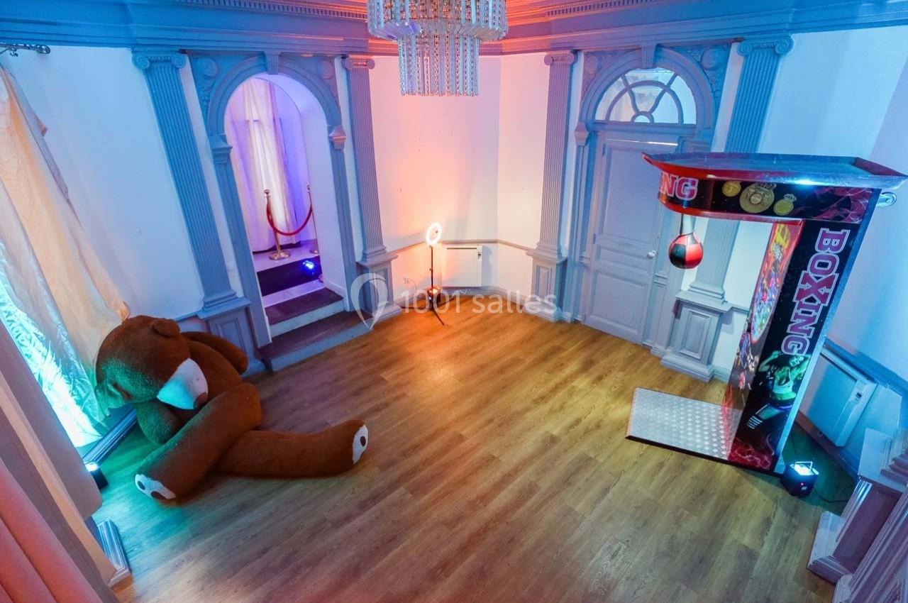 Salle avec un sol en bois, un grand ours en peluche, une machine de boxe et un éclairage coloré.