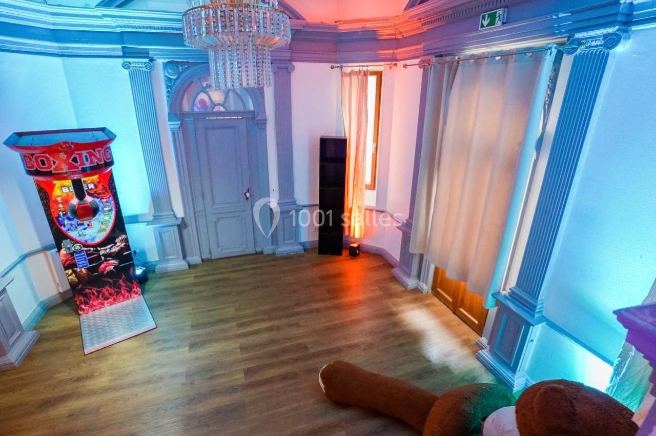 Salle lumineuse avec parquet, machine de boxe, rideaux beige, et éclairage coloré sur les murs.