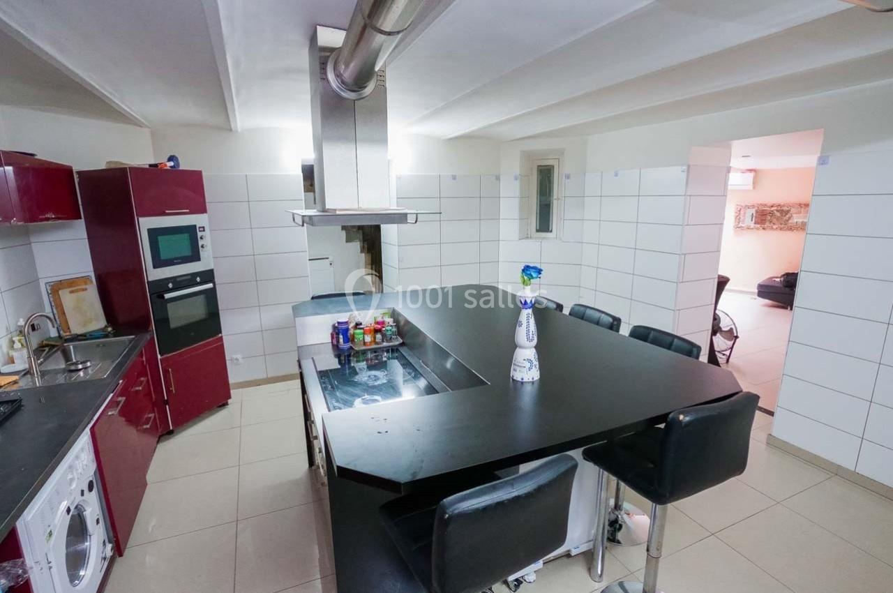 Cuisine moderne avec îlot central noir, chaises hautes, meubles rouges, électroménagers intégrés et carrelage blanc.