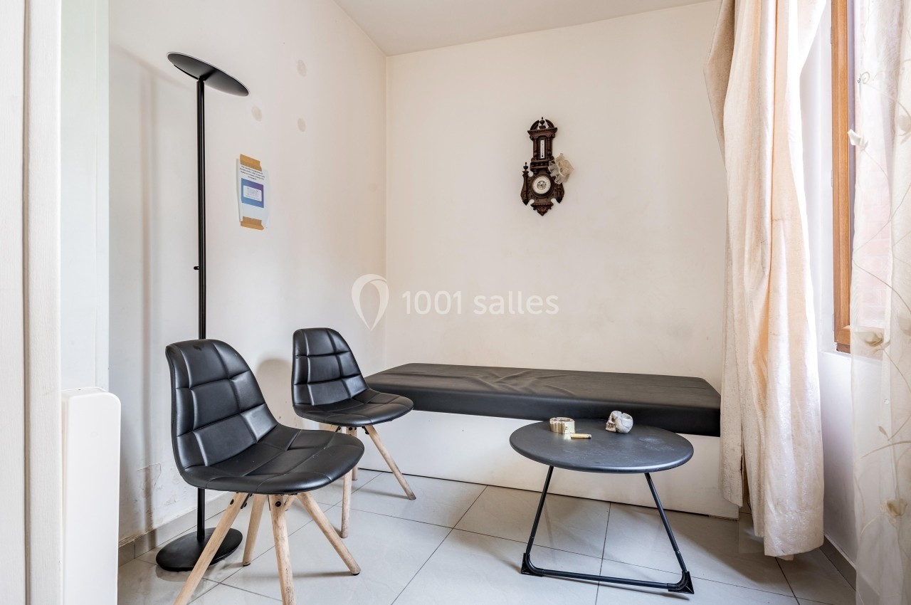 Coin salon minimaliste avec deux chaises noires, une table basse, un canapé, une horloge murale et une fenêtre avec rideaux.