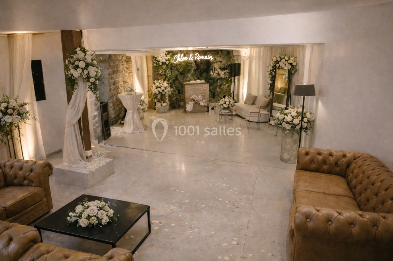 Salle de réception décorée avec des fleurs blanches, des canapés en cuir et un panneau lumineux en arrière-plan.