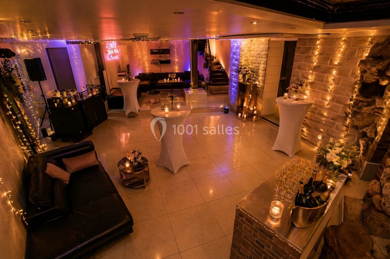 Salle décorée pour un événement, avec tables hautes, guirlandes lumineuses et ambiance chaleureuse.