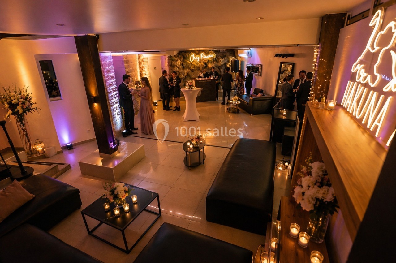 Salle de réception chaleureuse avec éclairage tamisé, décor floral, bougies et invités discutant près du bar.