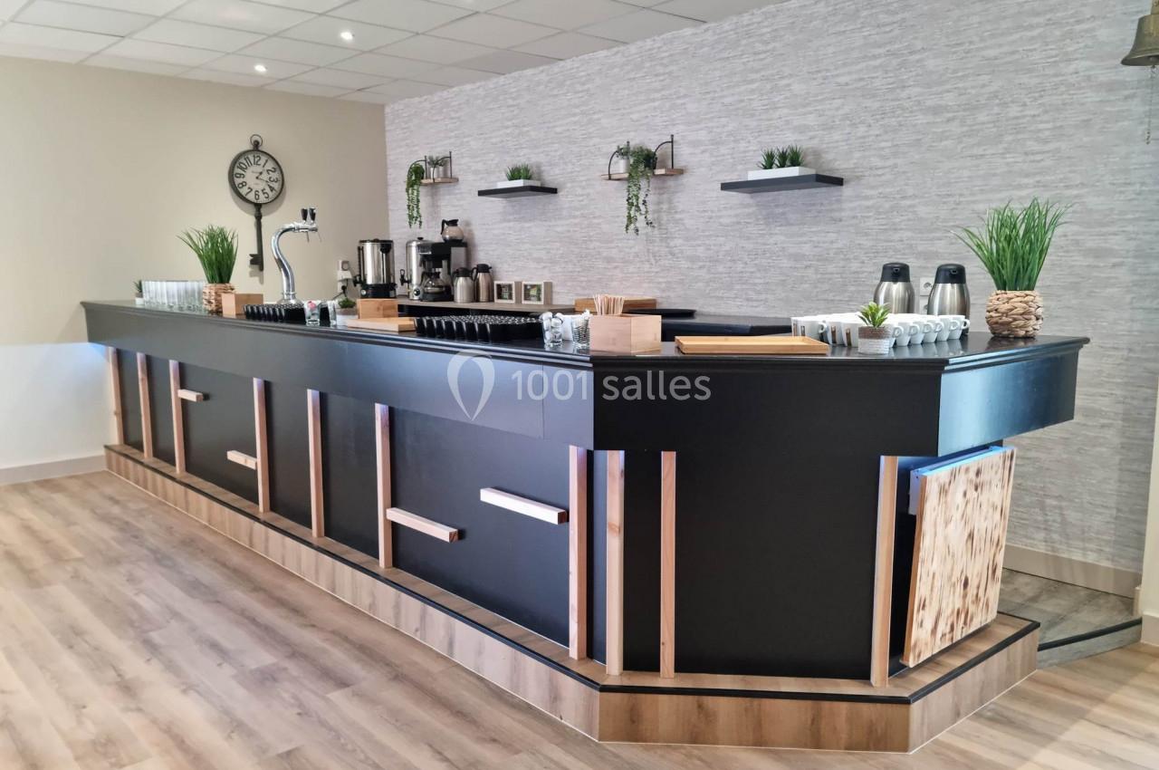 Comptoir moderne en bois et métal noir, équipé de machines à café, étagères décorées et plantes vertes.