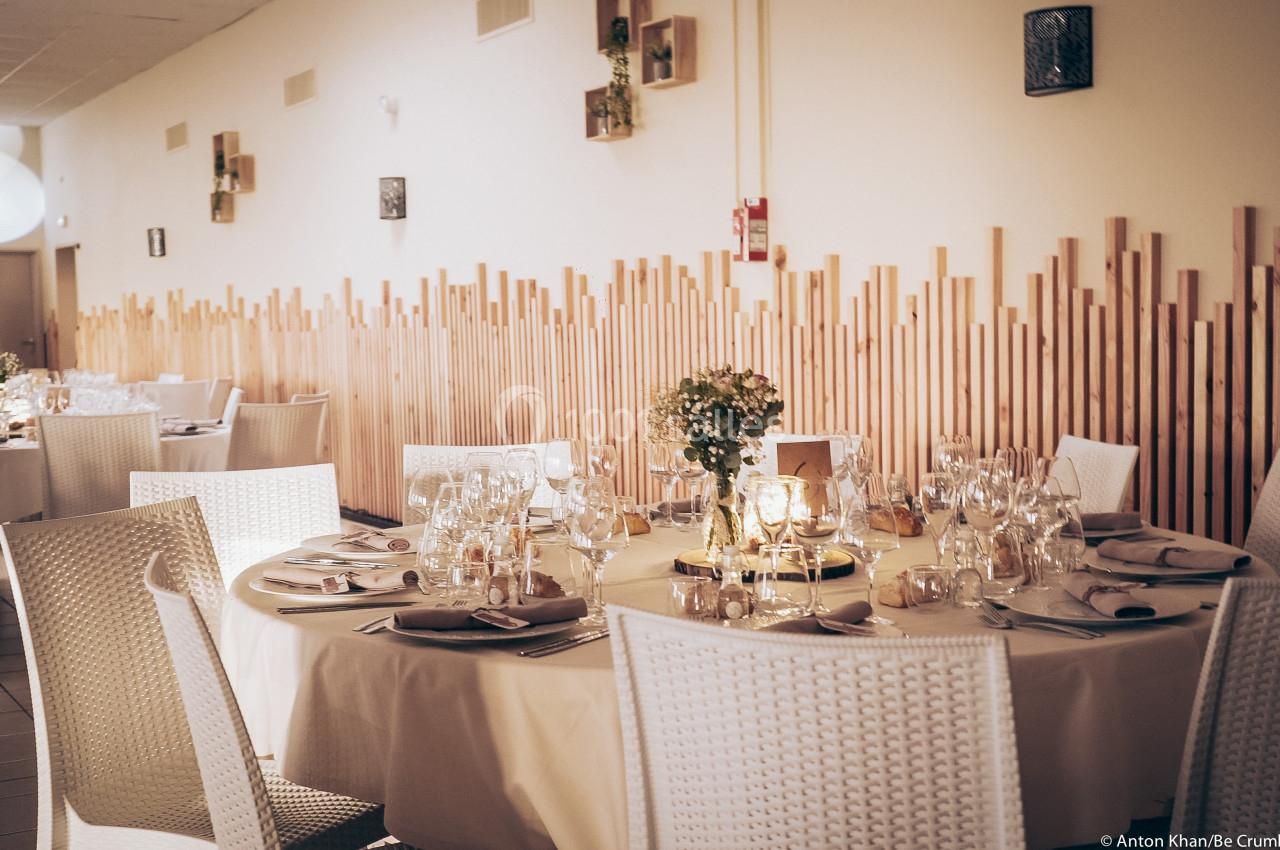 Salle de réception élégamment décorée avec des tables rondes dressées, chaises blanches et éclairage chaleureux.