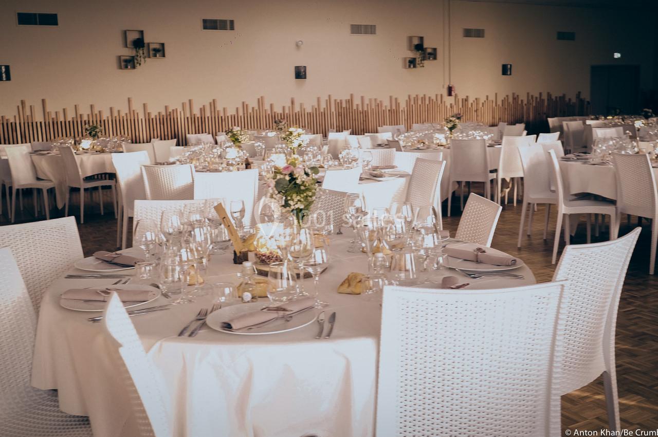 Salle de réception décorée avec des tables rondes dressées, nappes blanches et compositions florales au centre.