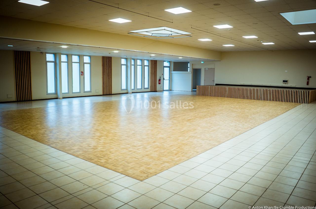 Salle spacieuse avec sol en parquet, bordée de carrelage, éclairée par des fenêtres et des luminaires au plafond.
