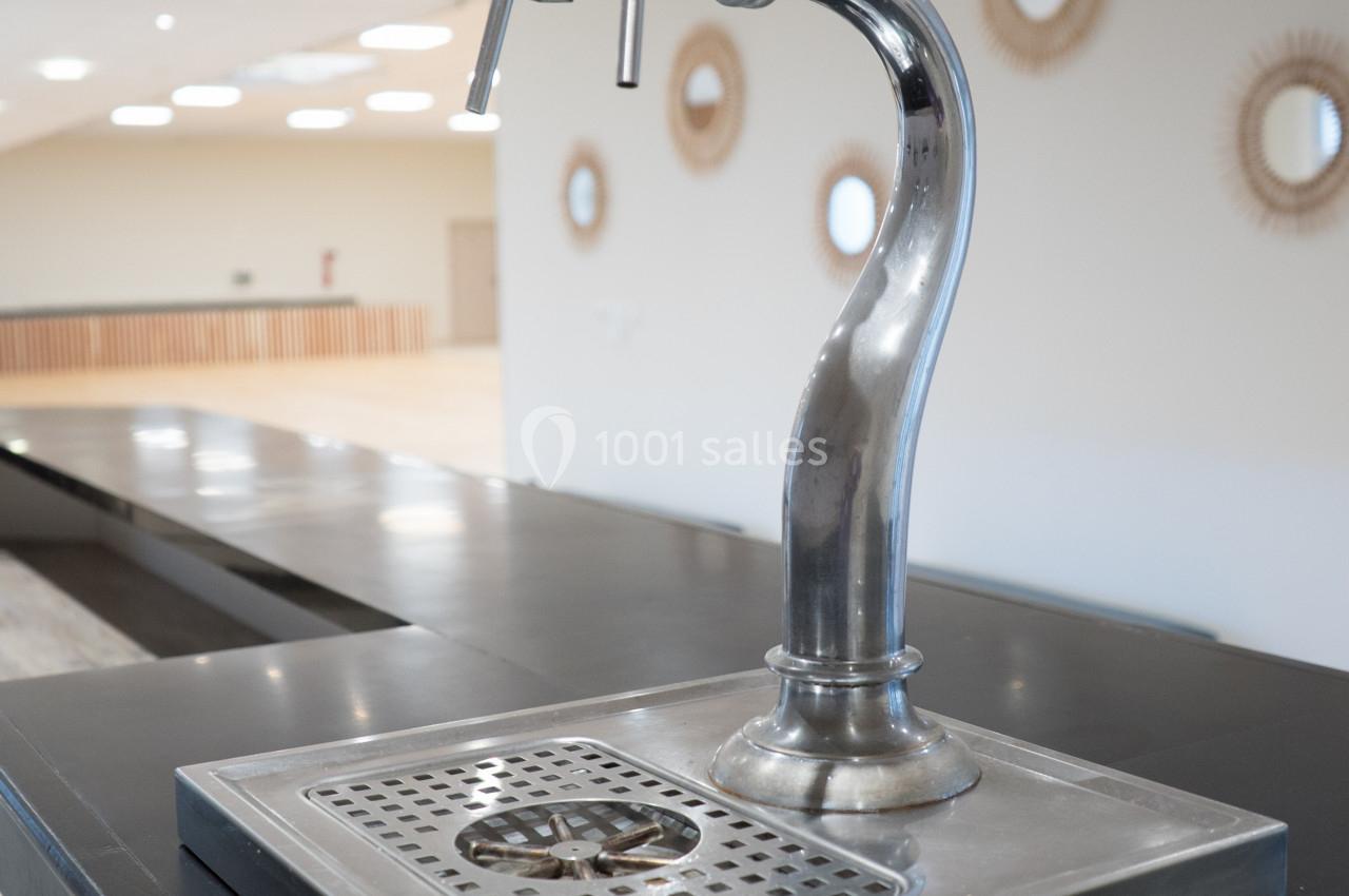 Robinet de distribution de boissons avec deux poignées noires, installé sur un comptoir en métal dans une salle lumineuse.