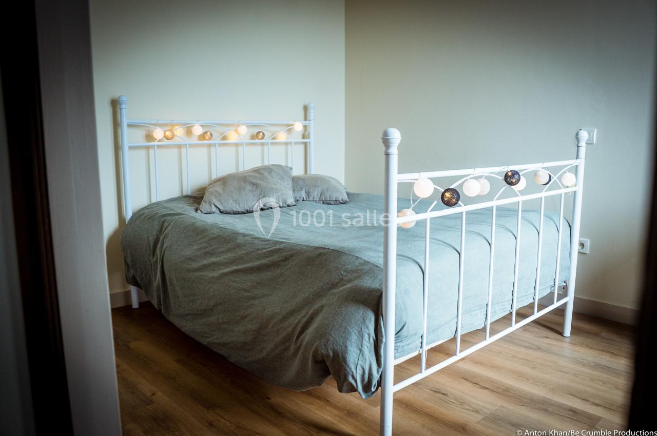 Lit en métal blanc avec une parure grise, décoré de guirlandes lumineuses, dans une chambre au sol en parquet.