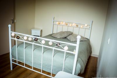 Lit double avec couvre-lit clair dans une chambre lumineuse, équipée d'une lampe sur pied et d'un lit superposé.