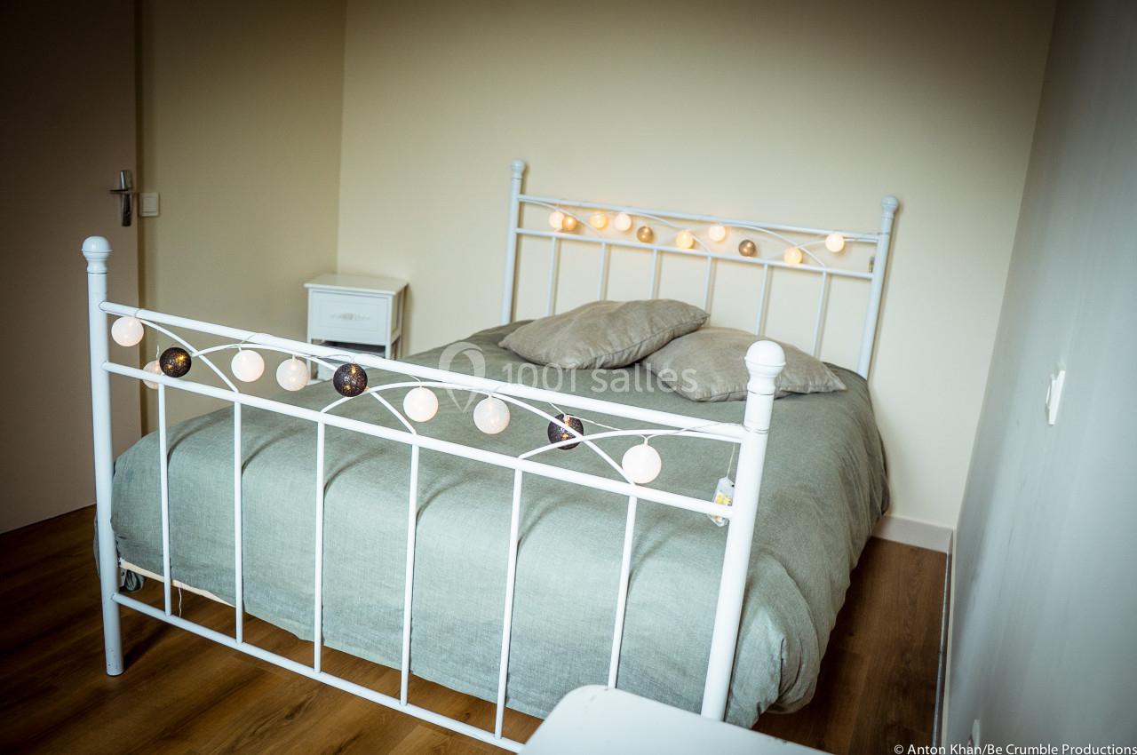 Lit double avec cadre en métal blanc décoré de guirlandes lumineuses, dans une chambre au sol en parquet.