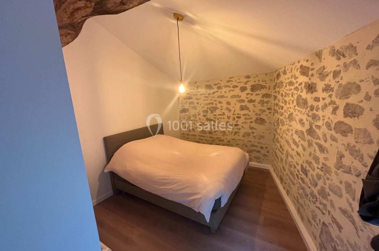 Chambre avec lit double, mur en pierre apparente, plafond mansardé et éclairage suspendu.