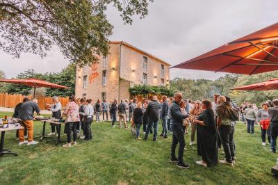 Groupe de personnes rassemblées sur une terrasse en bord de rivière, entourée de verdure et décorée de guirlandes lumineuses.