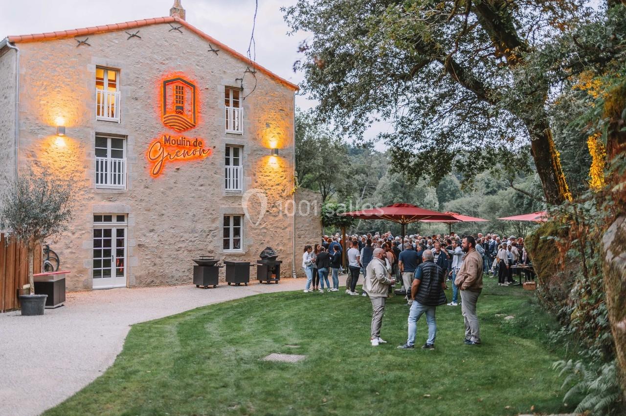 Groupe de personnes rassemblées devant un bâtiment en pierre éclairé, entouré d'arbres et de parasols rouges.