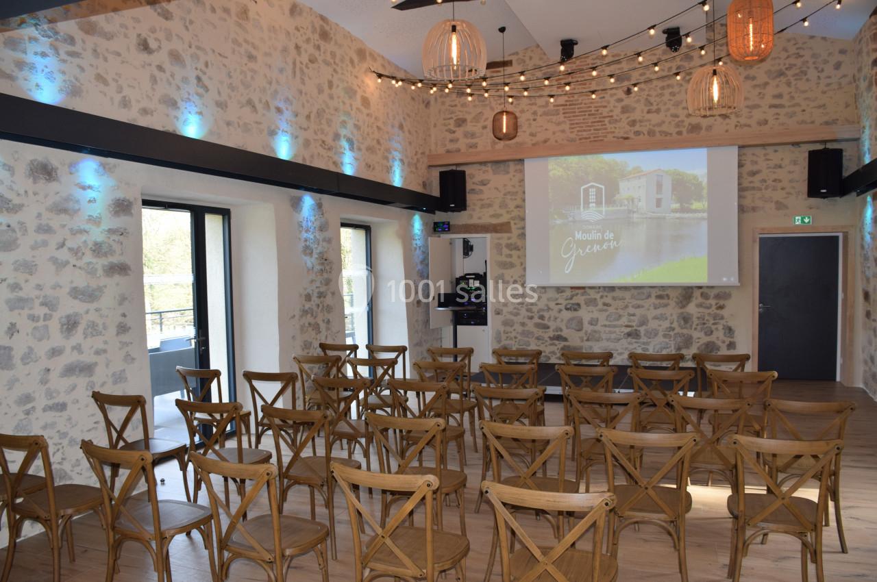 Salle de réunion en pierre avec chaises en bois, projecteur allumé et éclairage décoratif suspendu.