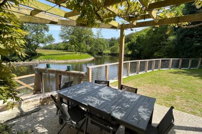 Groupe de personnes rassemblées sur une terrasse en bord de rivière, entourée de verdure et décorée de guirlandes lumineuses.